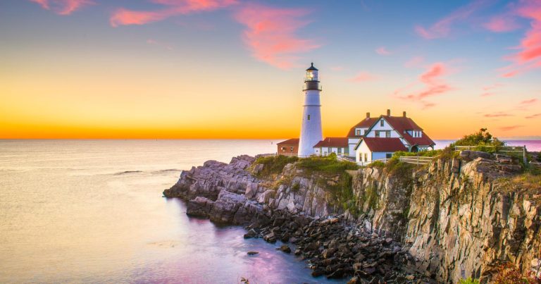 Maine landscape with lighthouse next to cliff at sunset