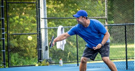 What Is Rally Scoring In Pickleball? Man hitting a pickleball backhand on an outdoor court