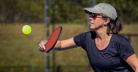 How to Hit A Killer Pickleball Backhand Serve Woman hitting a pickleball backhand serve