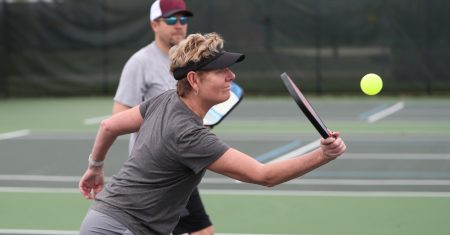Woman with visor playing pickleball on an outdoor court